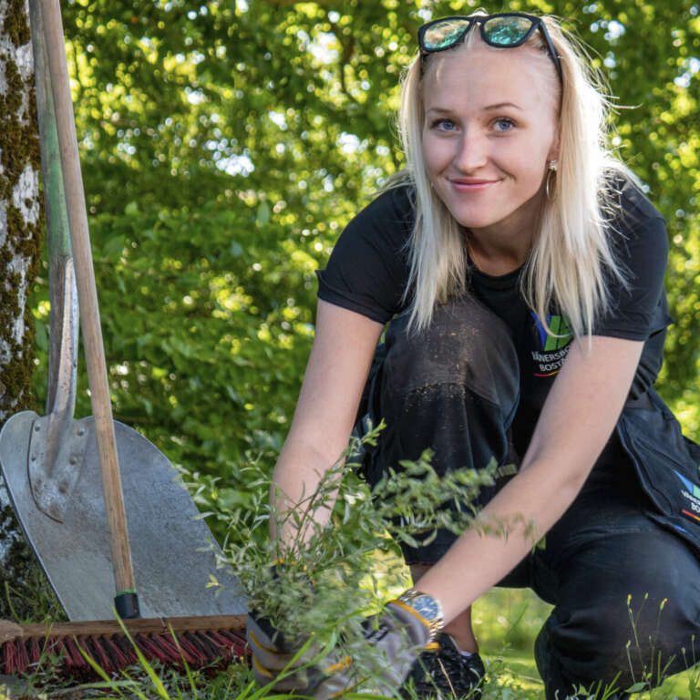 Natalie sitter ner på marken och planterar en växt.