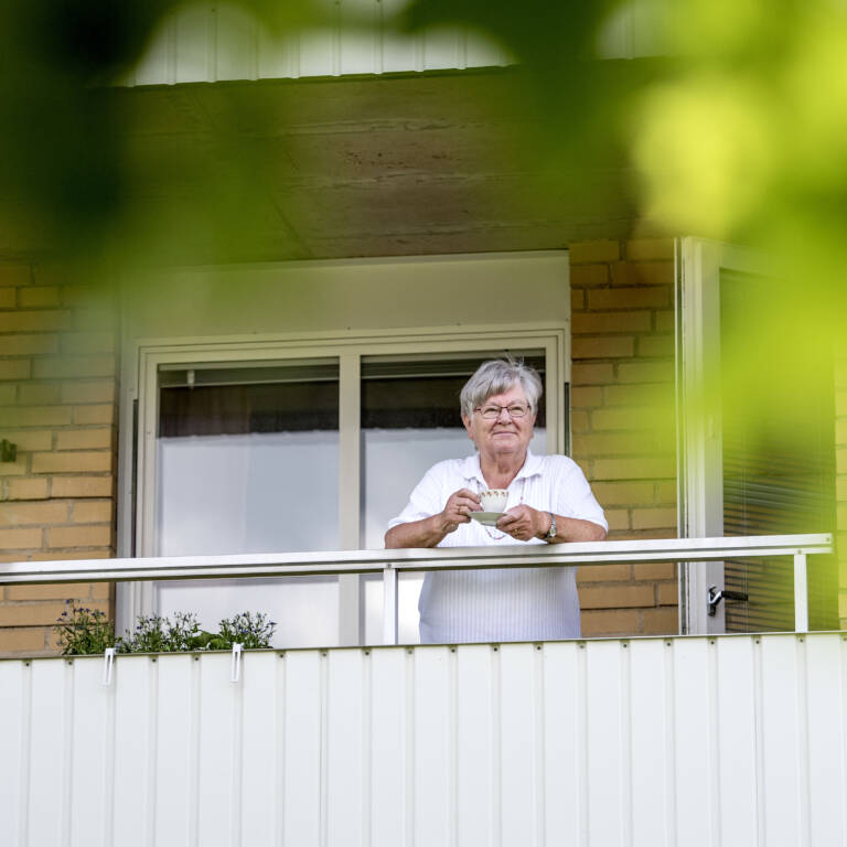 En äldre kvinna står på en balkong.