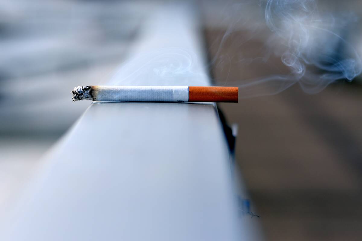 En cigarett ligger på ett räcke. Den glöder och ryker.