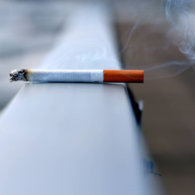 En cigarett ligger på ett räcke. Den glöder och ryker.