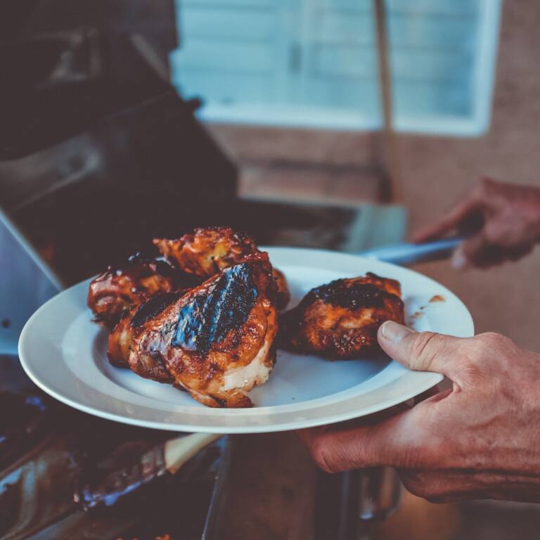 Grillad kyckling upplagd på en tallrik. I bakgrunden syns en grill.