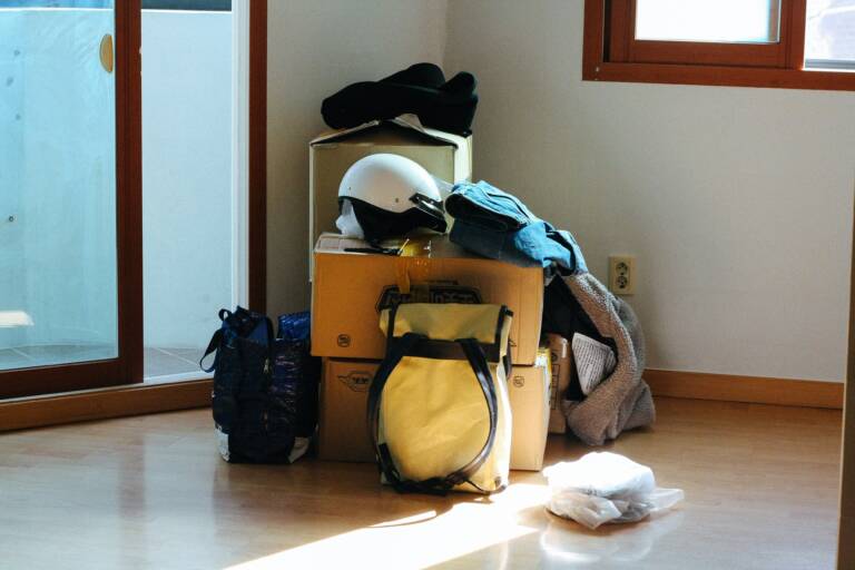 Flyttkartonger och väskor står på golvet i ett rum.