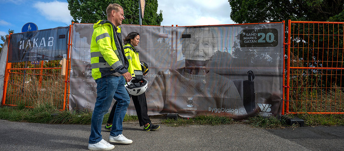 Peter och Nadja promenerar utanför byggstaketet på Sandmarksgatan 20.